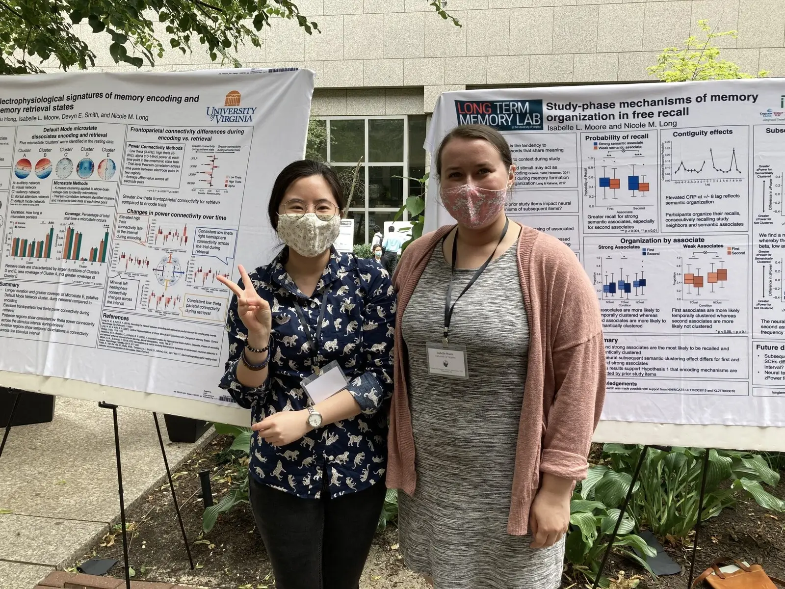 Two researchers in face masks standing among freestanding poster boards at a conference