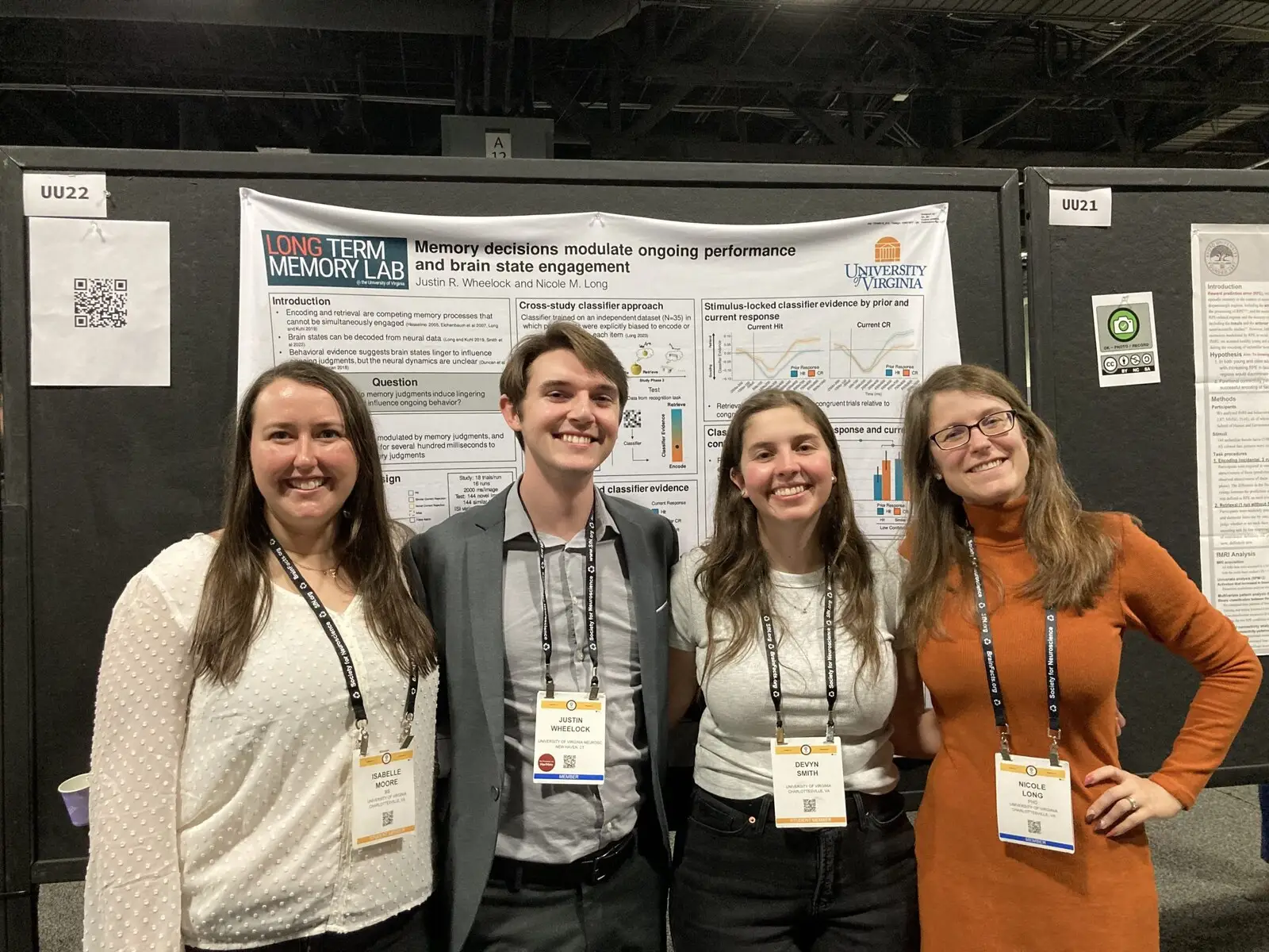 Four researchers wearing conference lanyards in front of a poster