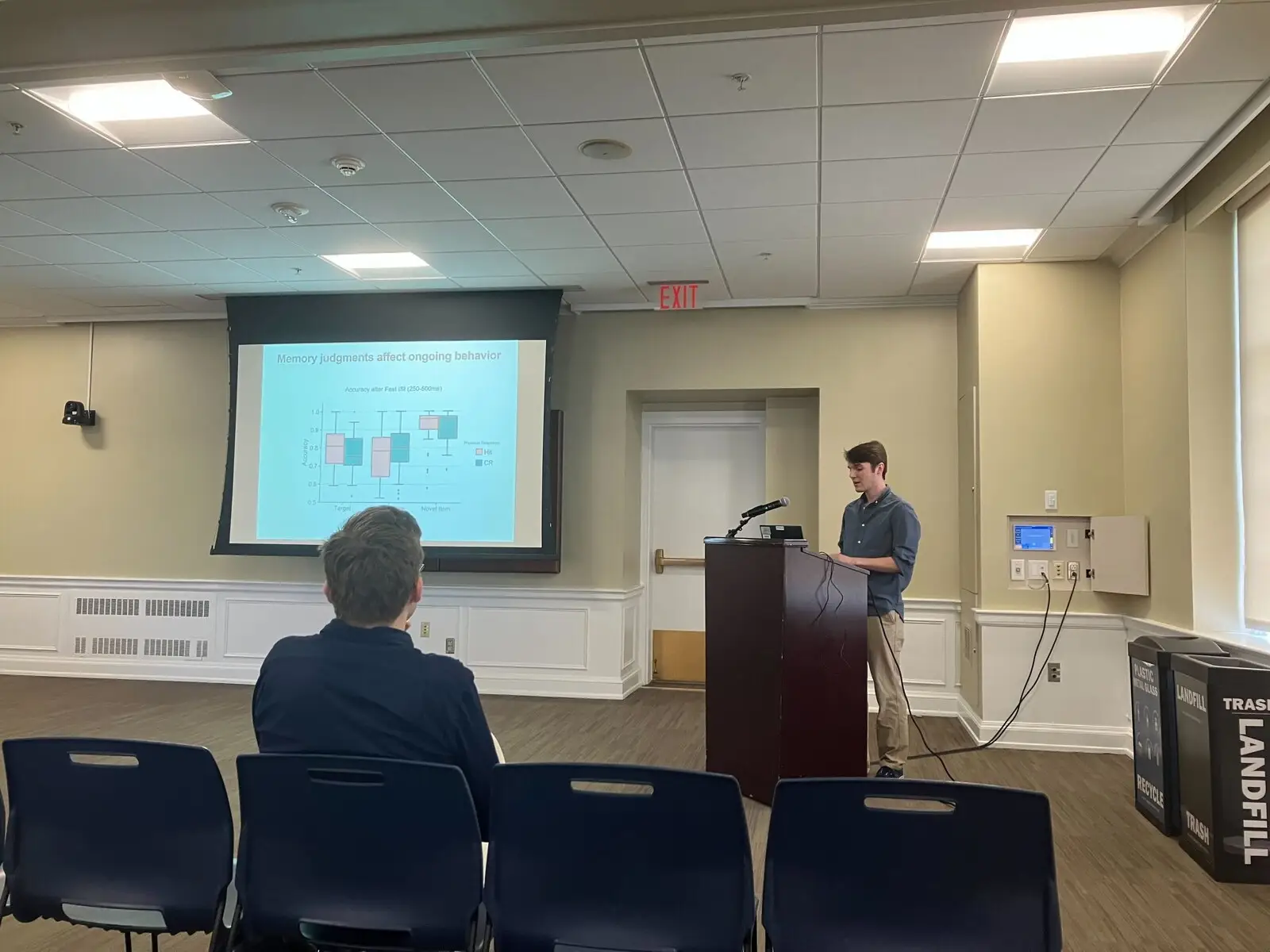 A student presenting from a lectern beside a projected slide in a seminar room