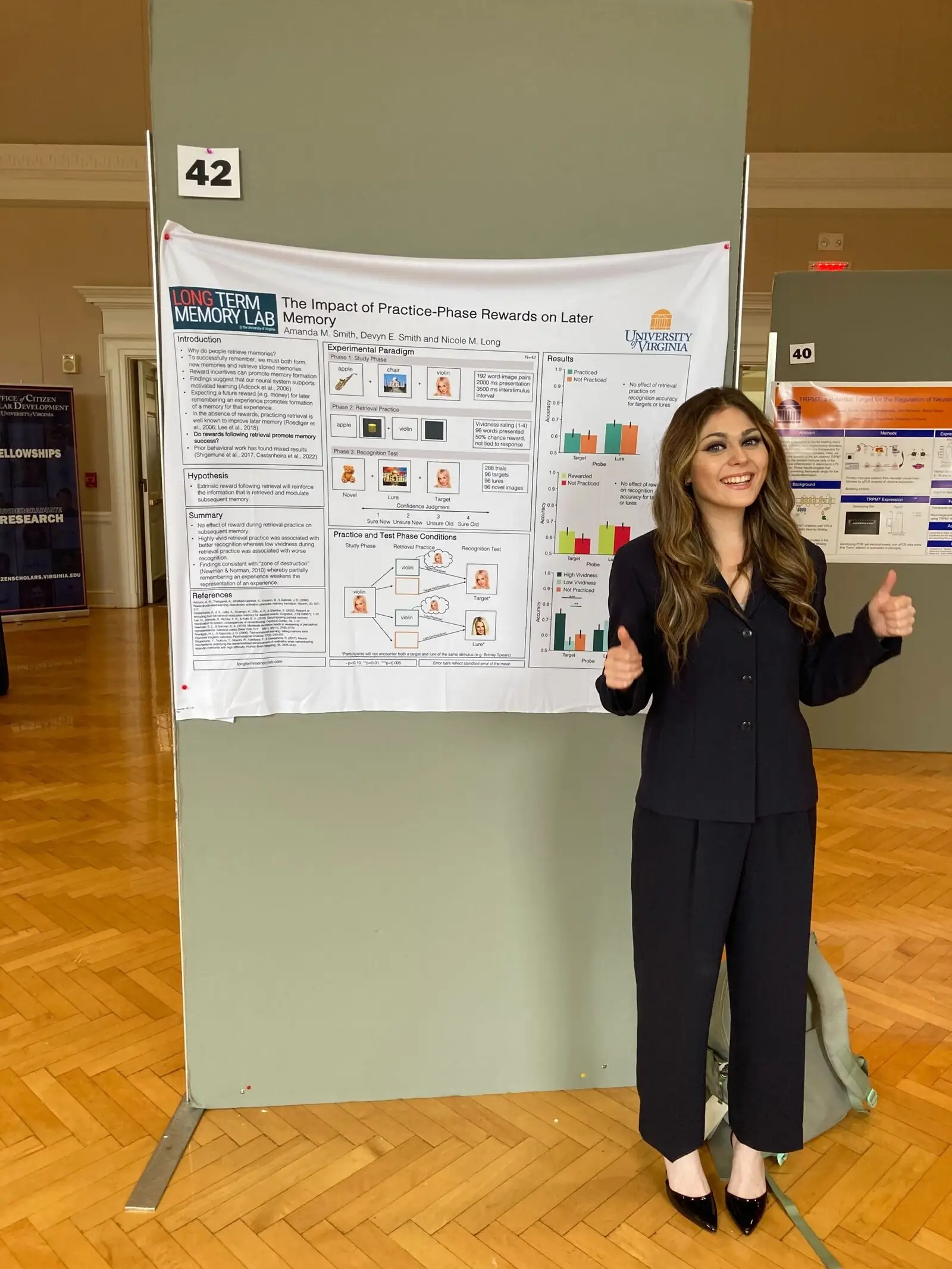A student standing beside her poster, giving a thumbs up