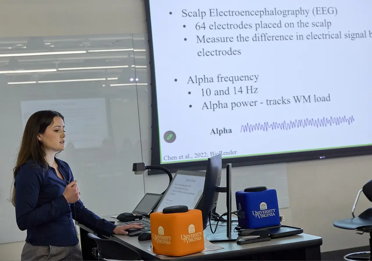 A projected slide describing scalp EEG methods and alpha frequency, beside a laptop on a desk