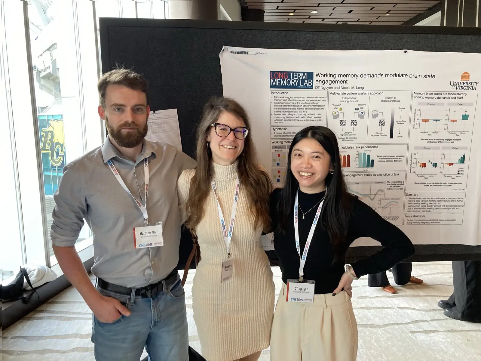 Three researchers standing in front of two posters at a conference